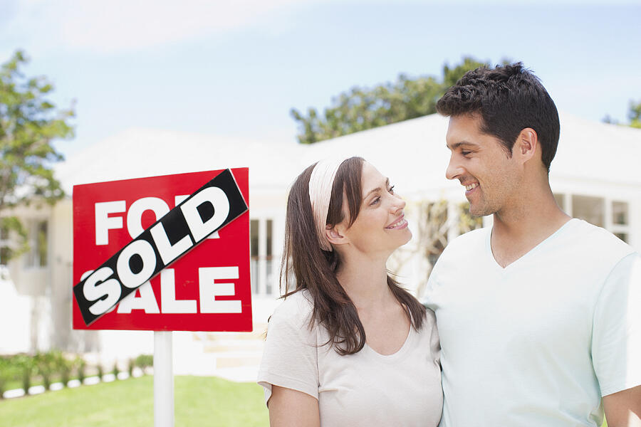 Couple standing near sold sign of their new house Photograph by Martin Barraud