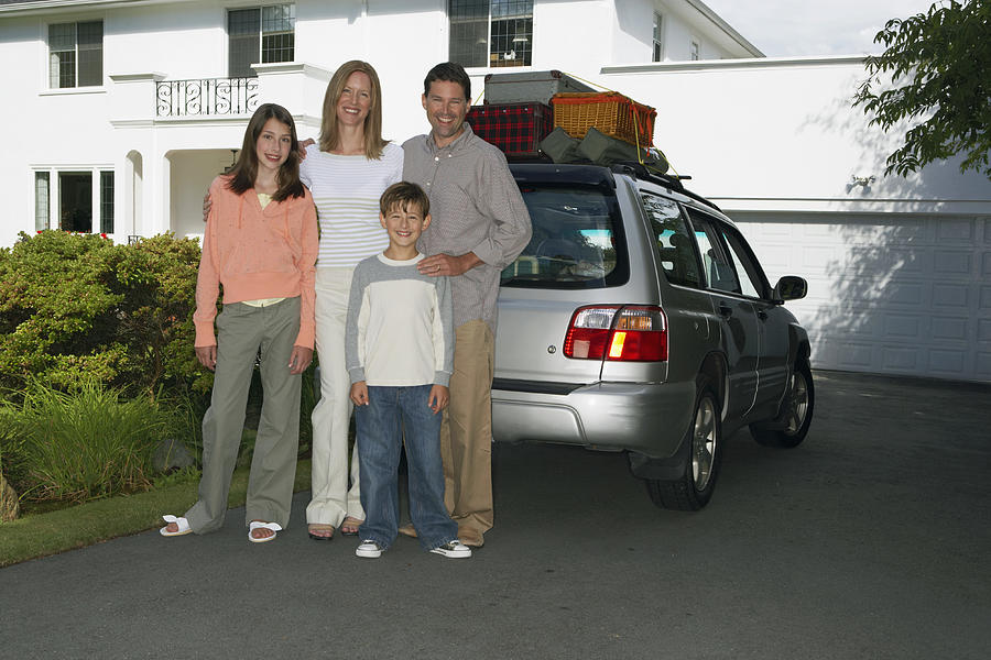 Couple standing with son and daughter (8-13 years) beside car in front drive Photograph by Noel Hendrickson