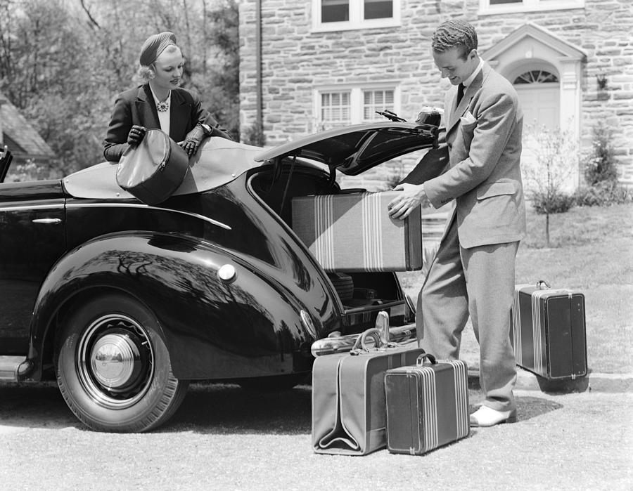 Couple. The Woman Looks On From The Back Seat Of A Covertible Coupe While The Man Is Loading A Set Of Luggage In The Trunk In Front Of A Stone Home. Photograph by H. Armstrong Roberts