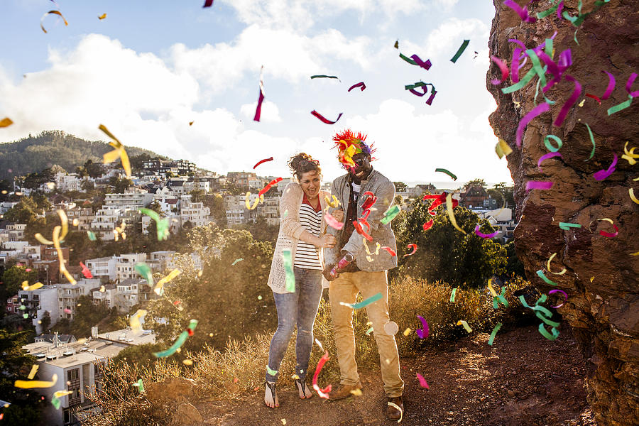 Couple throwing confetti on hill overlooking cityscape Photograph by Adam Hester