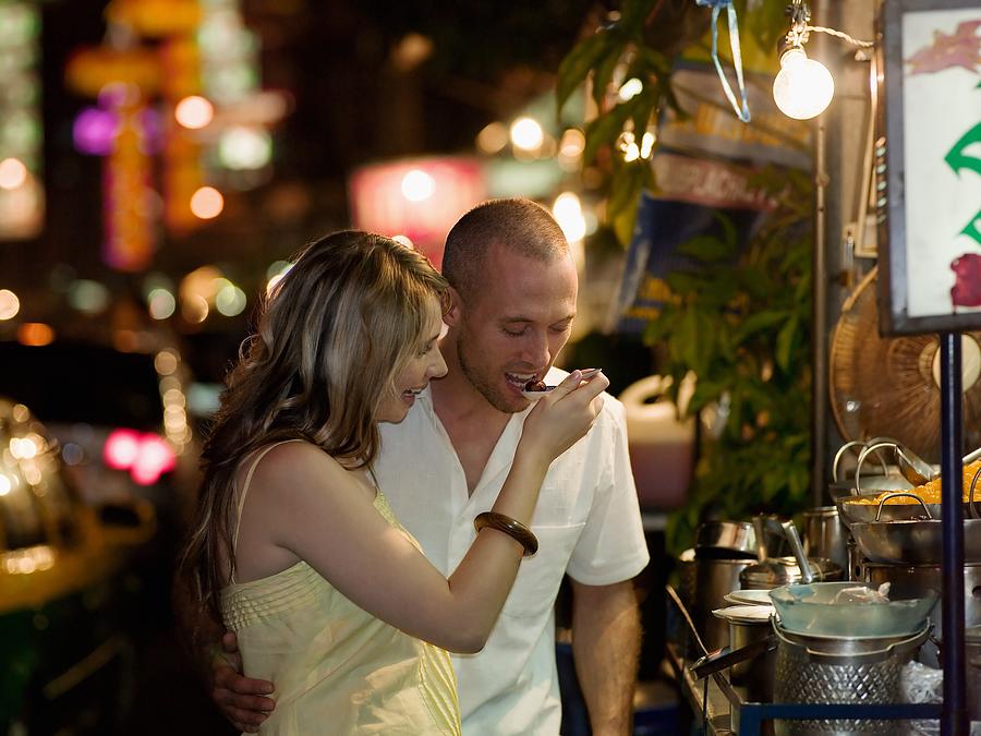 Couple trying food from street vendor Photograph by Image Source