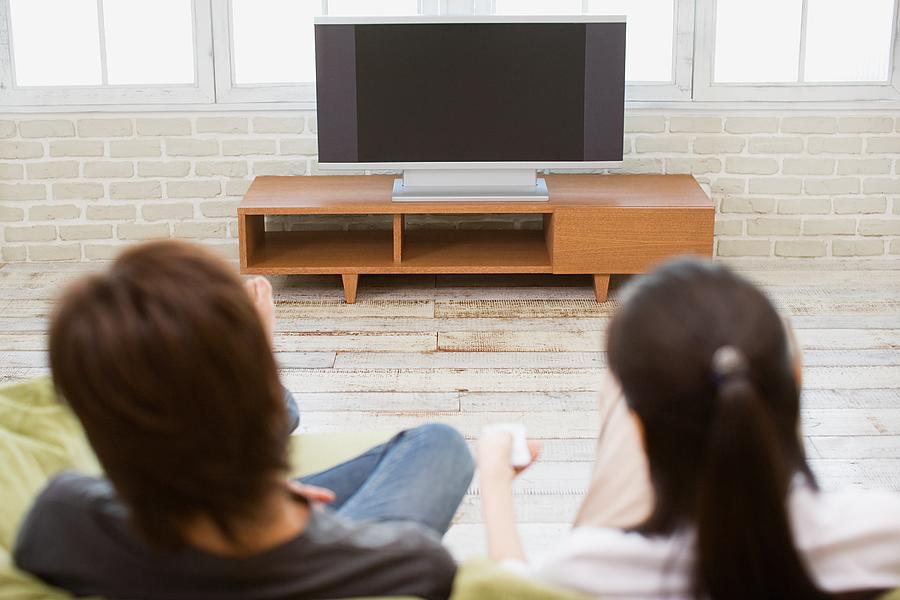 Couple turning television on Photograph by Image Source