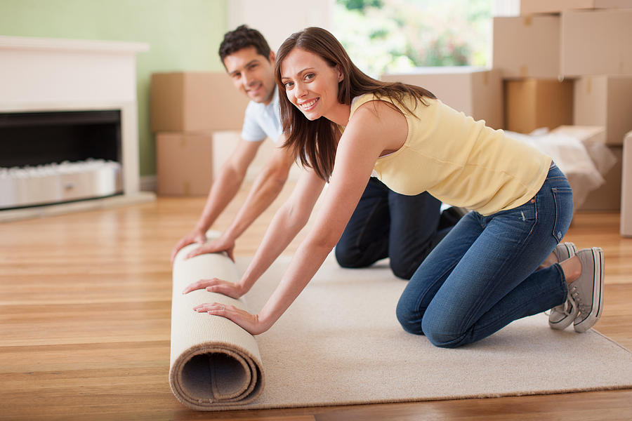 Couple unrolling carpet in new house Photograph by Paul Bradbury