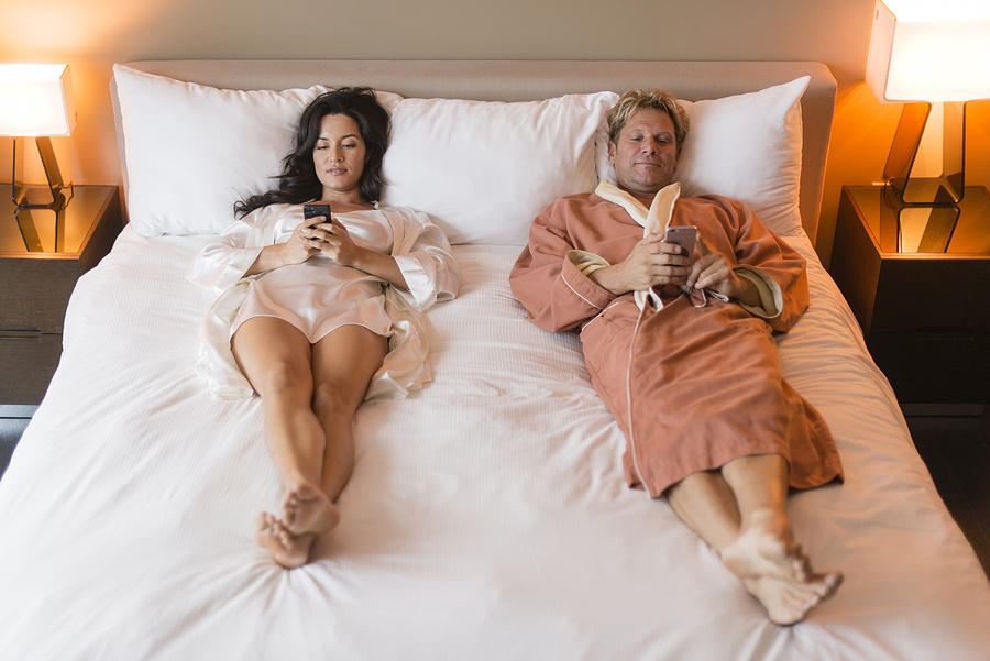 Couple using cell phones on bed Photograph by Rick Gomez