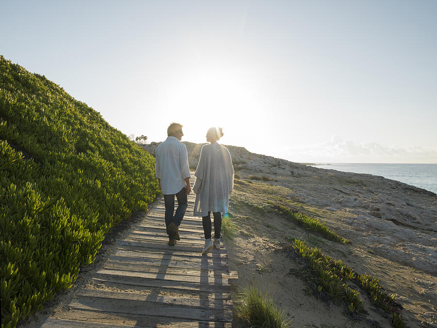 Couple walk along boardwalk above sea, talking Photograph by Ascent/PKS Media Inc.