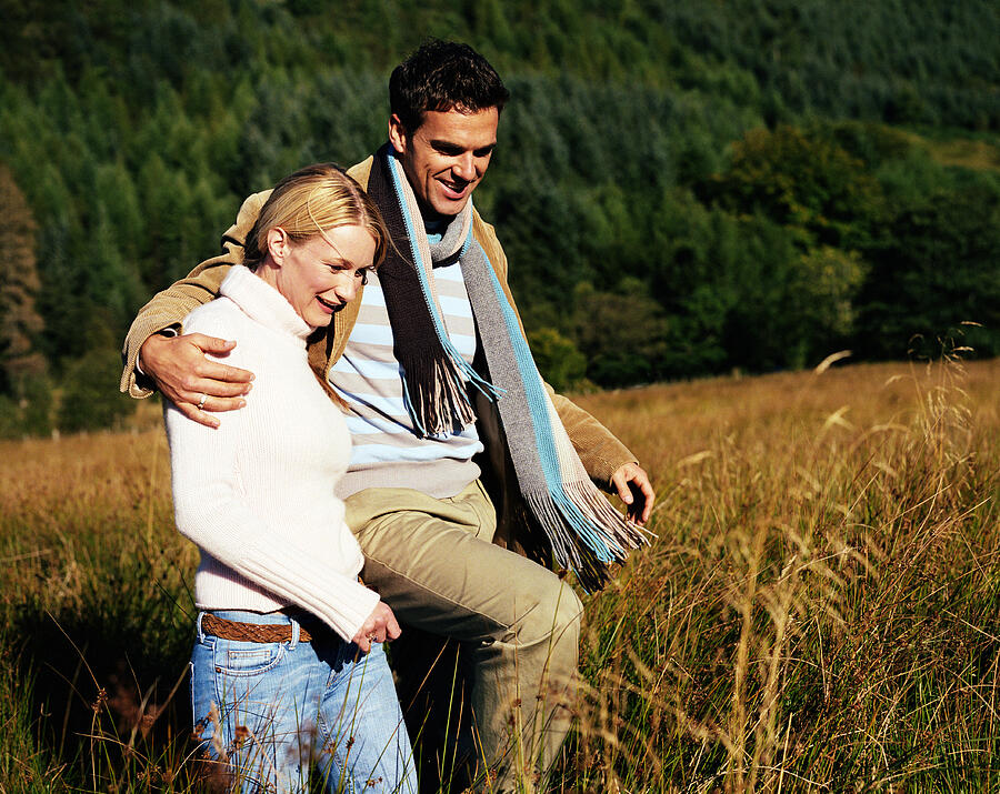 Couple walking arm and arm through long grass, smiling Photograph by Digital Vision