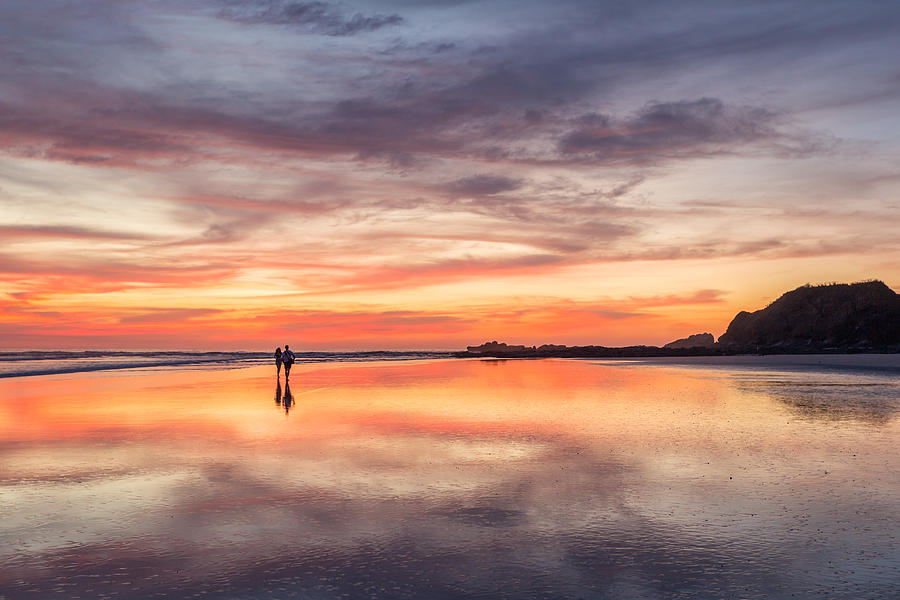 Couple walking on beach at sunset, Costa Rica Photograph by Matteo Colombo