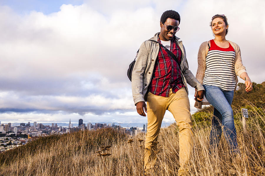 Couple walking on grassy hill overlooking cityscape Photograph by Adam Hester