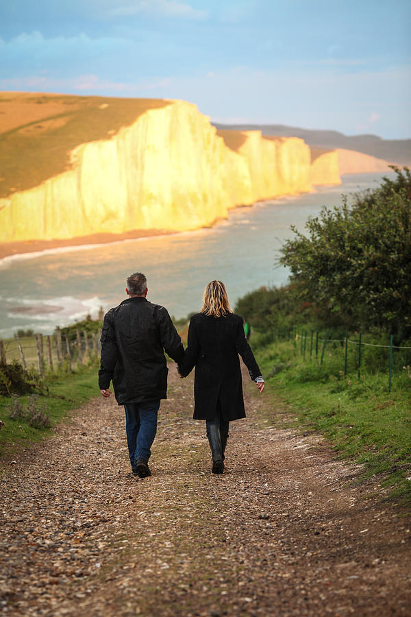Couple walking towards cliff coastline Photograph by Paul Mansfield Photography