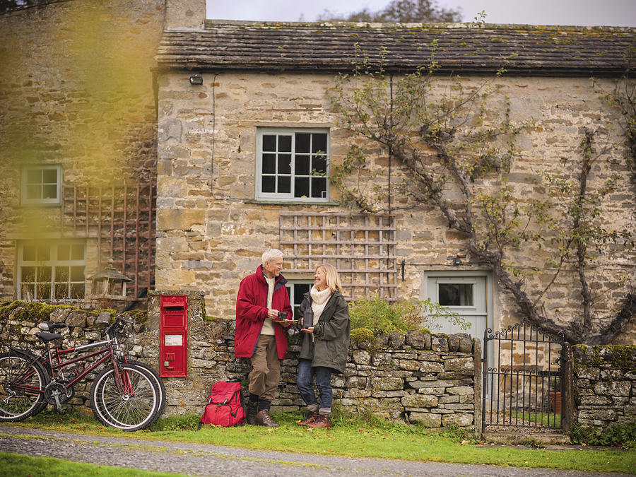 Couple with bicycles standing by dry stone wall and cottage in rural village Photograph by Monty Rakusen