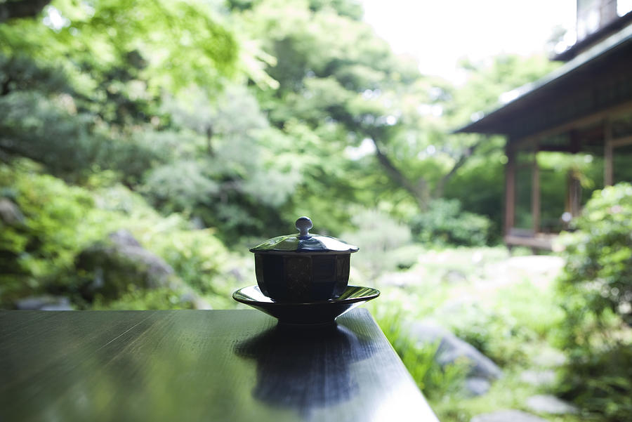 Covered tea cup and saucer on table, Japanese garden in background Photograph by ZenShui/Laurence Mouton