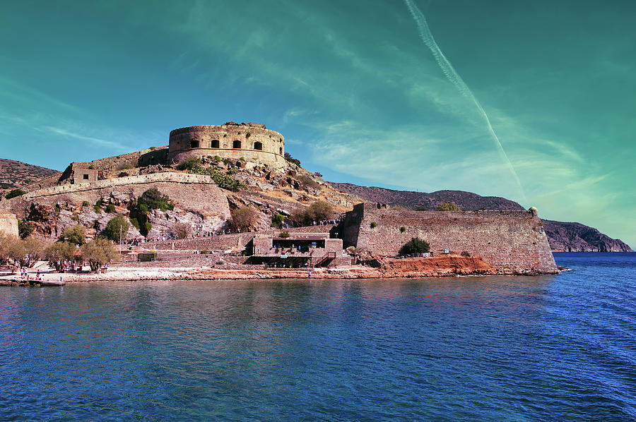 Crete, Greece Wide angle view of Spinalonga unhabited island with a 16th century venetian fortress and the ruins of a formar leper colony against cloudy blue sky and blue water in the foreground Photograph by Arpan Bhatia