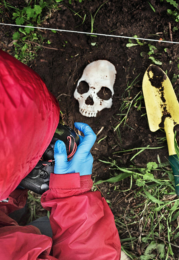 Crime scene investigator photographing disinterred human skull Photograph by RapidEye