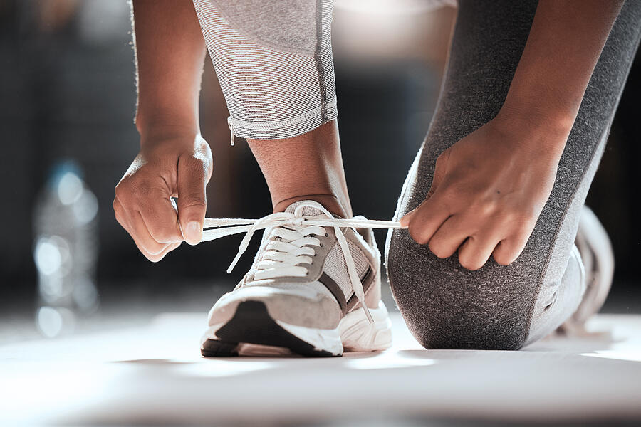 Cropped shot of an unrecognizable woman tying her shoelaces while exercising at the gym Photograph by PeopleImages