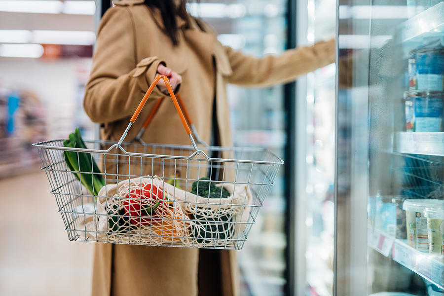 Cropped shot of woman carrying shopping basket and shopping groceries in supermarket Photograph by Oscar Wong