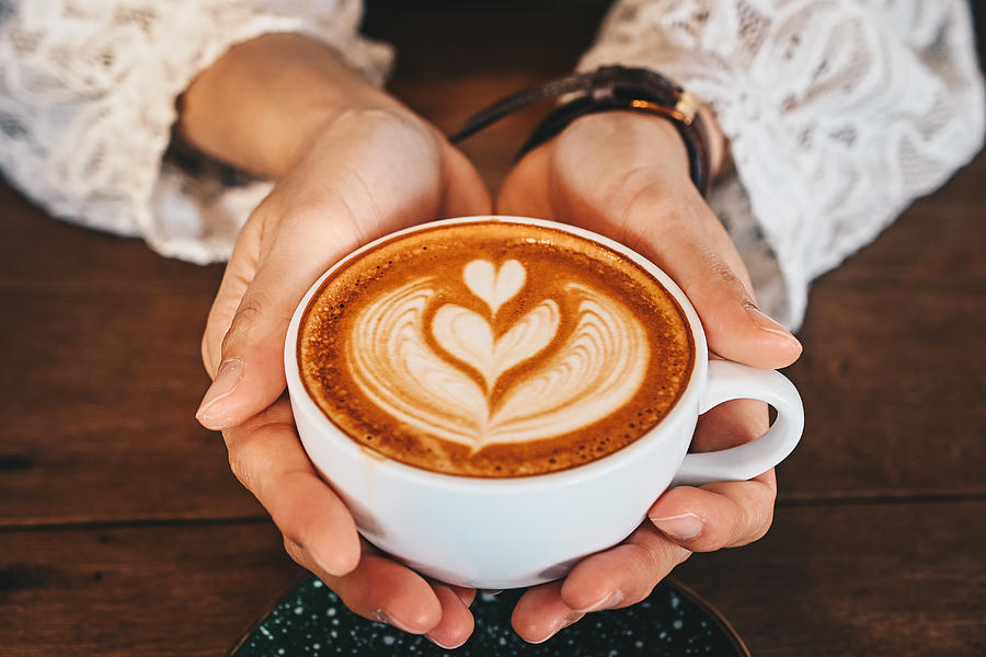 Cropped shot of woman hands holding a cup of hot latte coffee in her hands. Photograph by Boy_Anupong