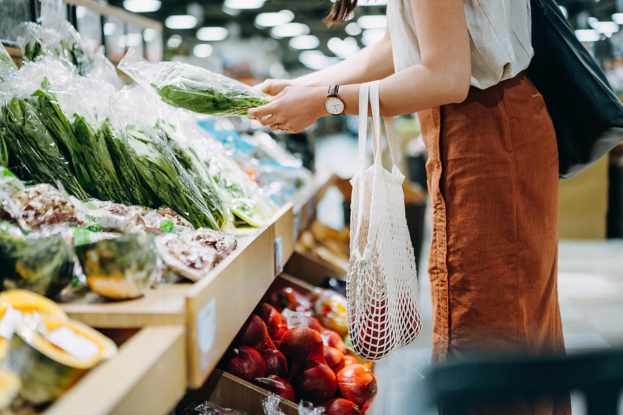 Cropped shot of young Asian woman shopping for fresh organic groceries in supermarket. She is shopping with a cotton mesh eco bag and carries a variety of fruits and vegetables. Zero waste concept Photograph by D3sign