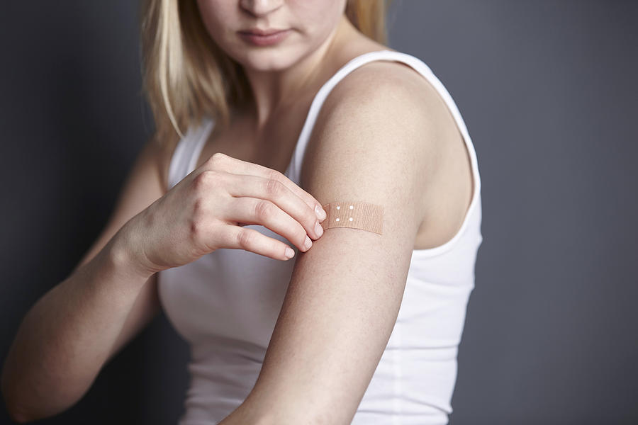 Cropped shot of young woman applying adhesive plaster to her own arm Photograph by Maria Fuchs