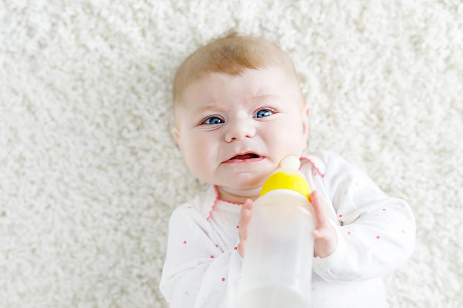 Cute adorable ewborn baby girl holding nursing bottle and drinking formula milk Photograph by Romrodinka