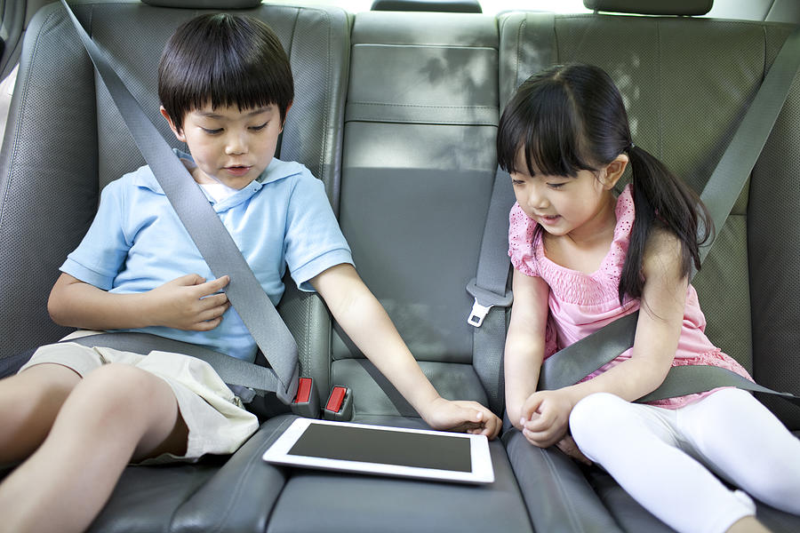Cute boy and girl playing digital tablet in car Photograph by BJI/Blue Jean Images