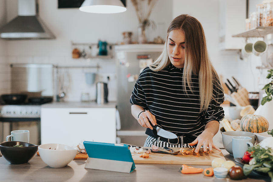 Cute female teenager cooks dinner while having a video call conversation Photograph by Visualspace