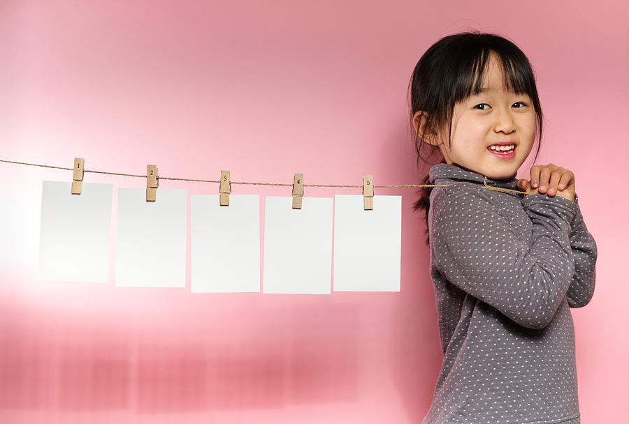Cute girl pulling a clothesline with five sheets of white paper Photograph by EujarimPhotography