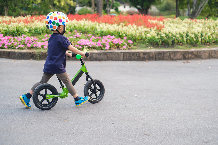 Cute little 2 - 3 years old toddler boy child wearing safety helmet learning to ride first balance bike in sunny summer day Photograph by Yaoinlove