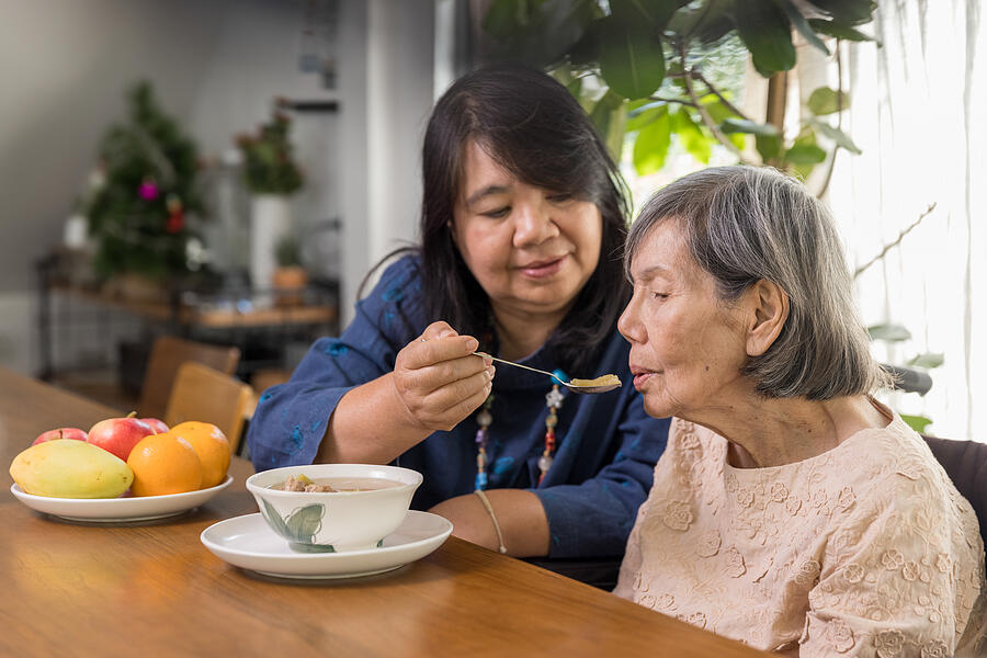 Daughter feeding elderly mother with soup. Photograph by Toa55