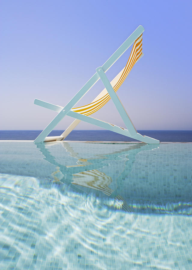 Deck chair on edge of pool Photograph by Peter Cade