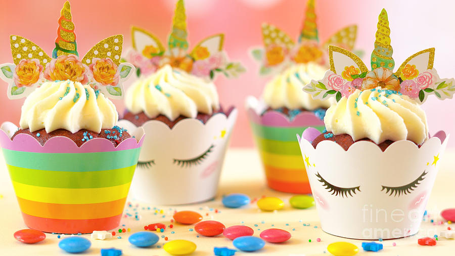 Decorating childrens birthday party unicorn themed cupcakes, closeup. Photograph by Milleflore Images