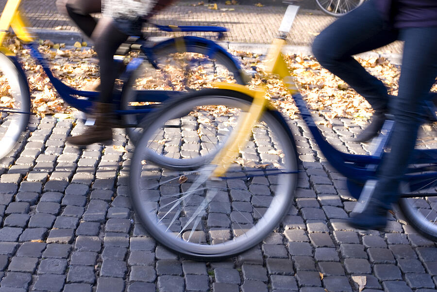 Defocused cyclists riding along Dutch cobbled street Photograph by Lyn Holly Coorg