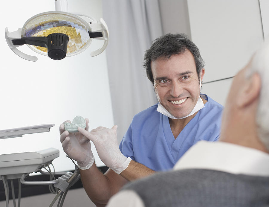 Dentist showing patient a mold of teeth and smiling Photograph by Sam Edwards