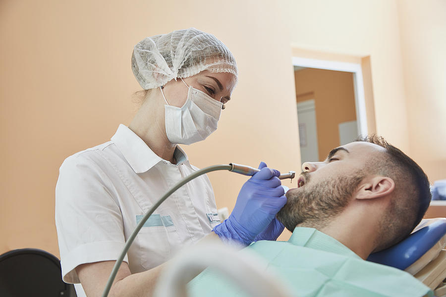 Dentist wearing surgical mask and cap while examining male patient Photograph by Alexandr Sherstobitov