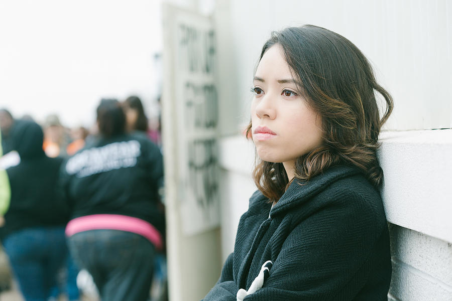 Depressed young woman standing in line at city food bank Photograph by SDI Productions