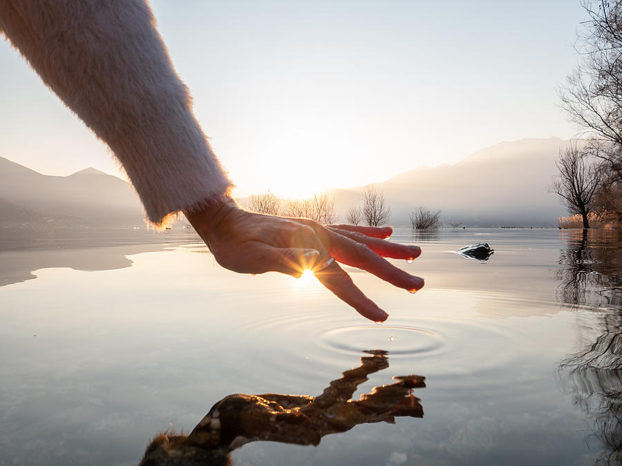 Detail of hand touching water surface of lake at sunset Photograph by Swissmediavision