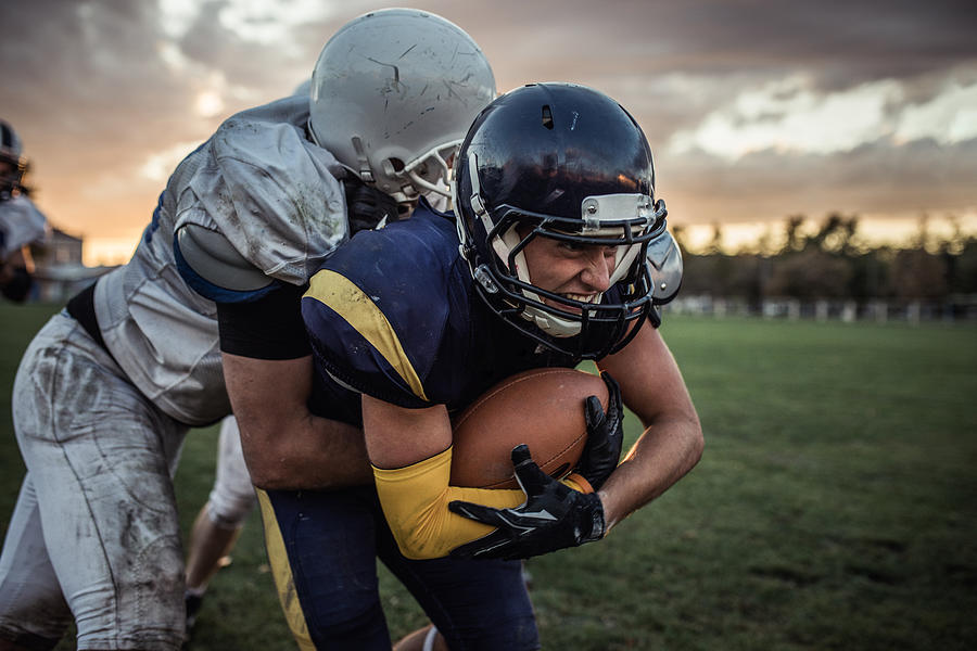 Determined American football player trying to pass defensive player on a match. Photograph by Skynesher