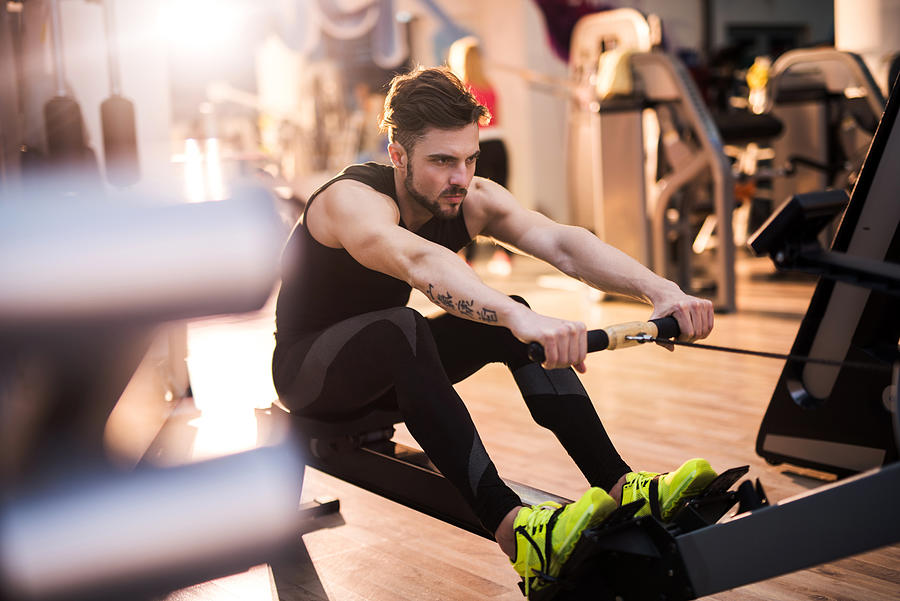 Determined man exercising on rowing machine in a gym. Photograph by BraunS