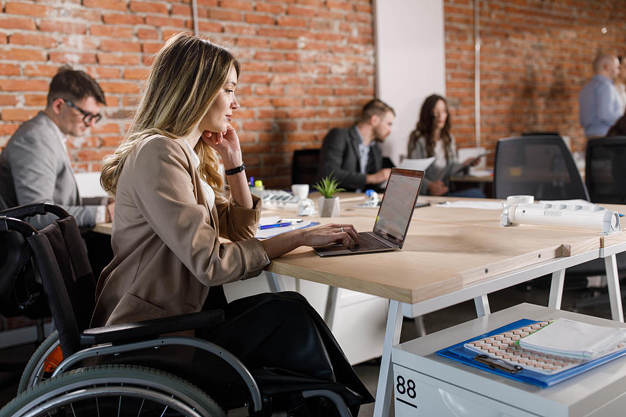Disabled businesswoman working on laptop in the office. Photograph by Skynesher