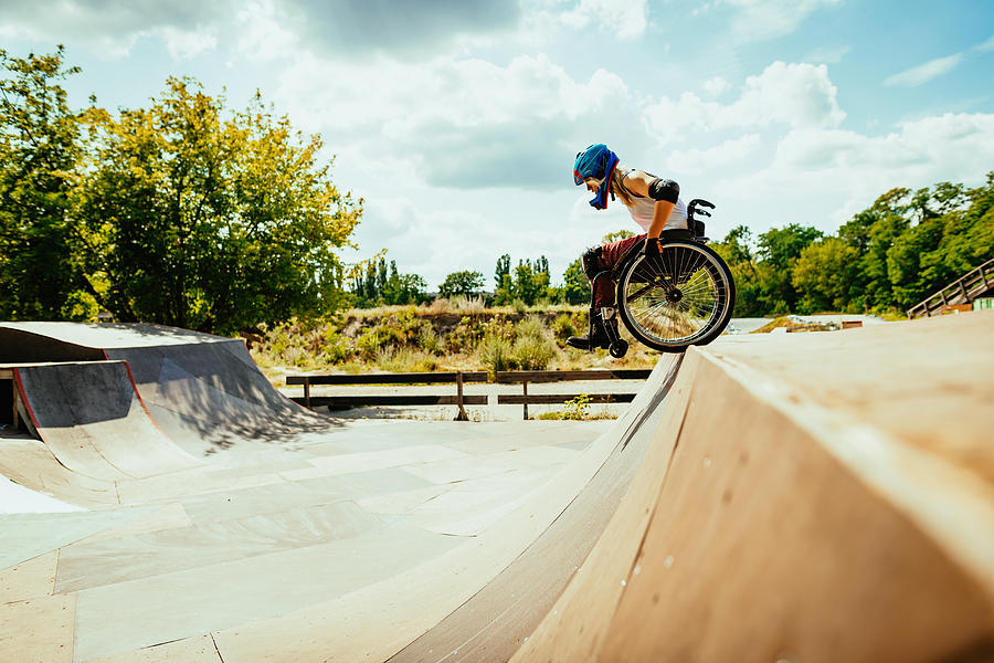 Disabled millennial woman in wheelchair rolls down the hills in skate park Photograph by Drazen_