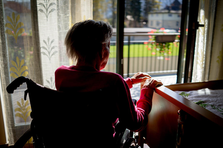 Disabled senior woman in wheelchair at home in living room Photograph by Jasmin Merdan