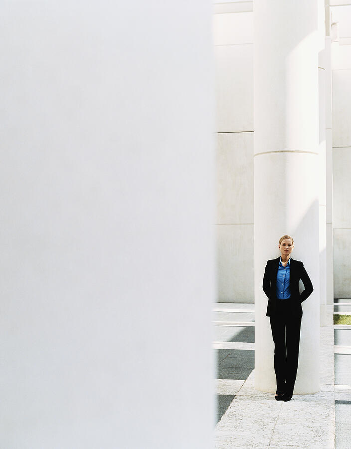 Distant View of a Businesswoman Leaning on a Pillar Photograph by Digital Vision.
