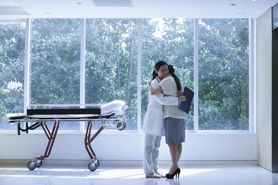 Doctor and patient hugging in a hospital next to a stretcher, full length Photograph by XiXinXing