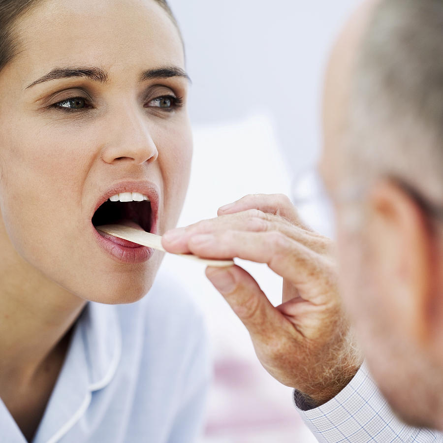Doctor Examining With A Woman With A Tongue Depressor Photograph by Stockbyte