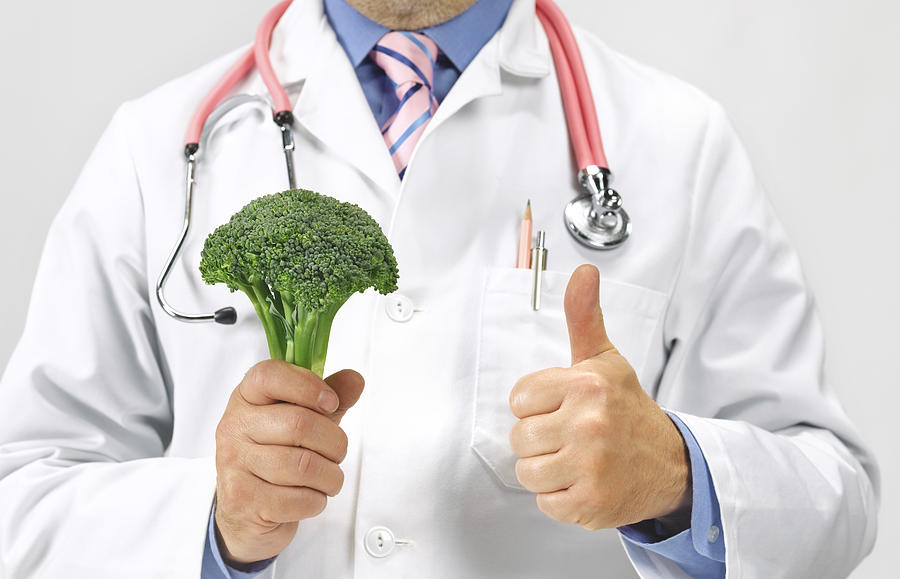 Doctor gives thumbs up to a floret of broccoli Photograph by Peter Dazeley
