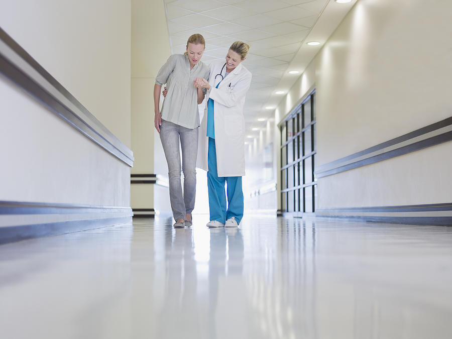 Doctor helping weak patient walk in corridor Photograph by Martin Barraud
