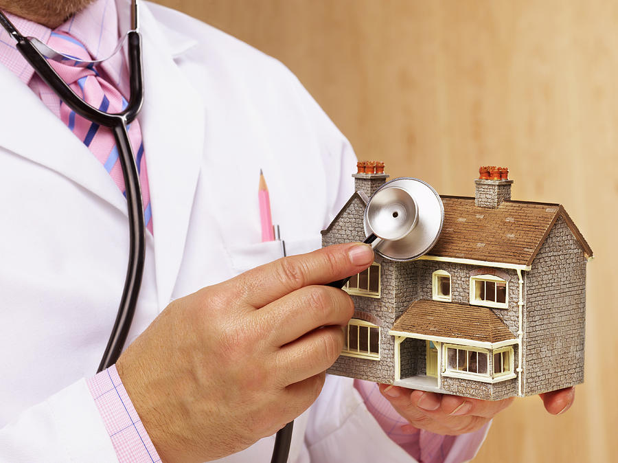 Doctor holding stethoscope to model house, mid section Photograph by Peter Dazeley