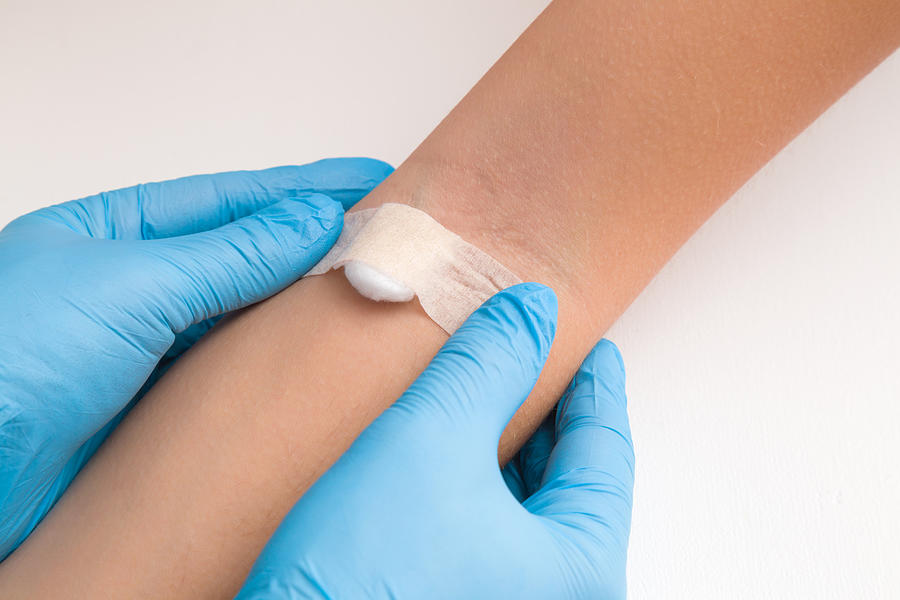 Doctor in blue rubber protective gloves putting an adhesive bandage on young womans arm vein after blood test or injection of vaccine. First aid. Medical, pharmacy and healthcare concept. Closeup. Photograph by FotoDuets