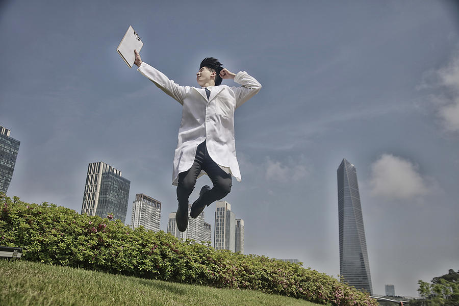 Doctor jumping up with clipboard Photograph by Runstudio