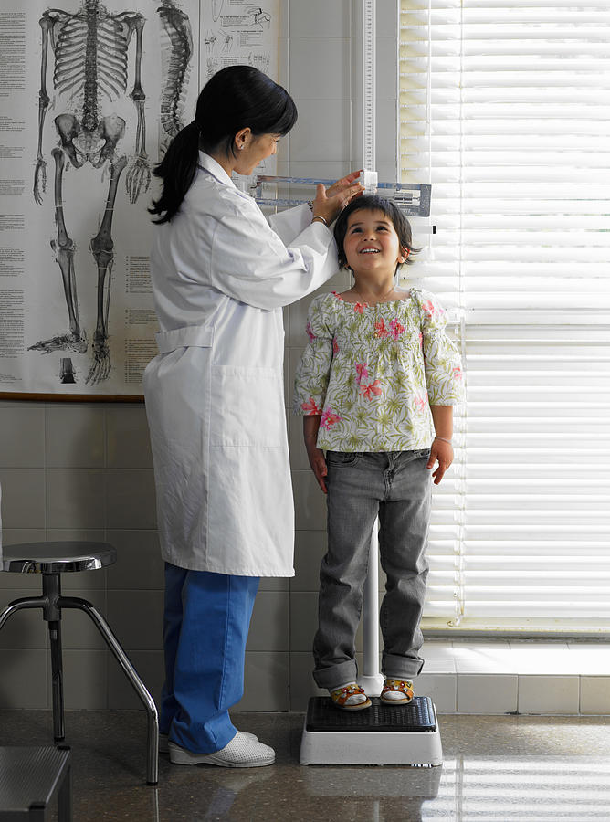 Doctor measuring girl (5-7 years) in examination room Photograph by Michael Blann