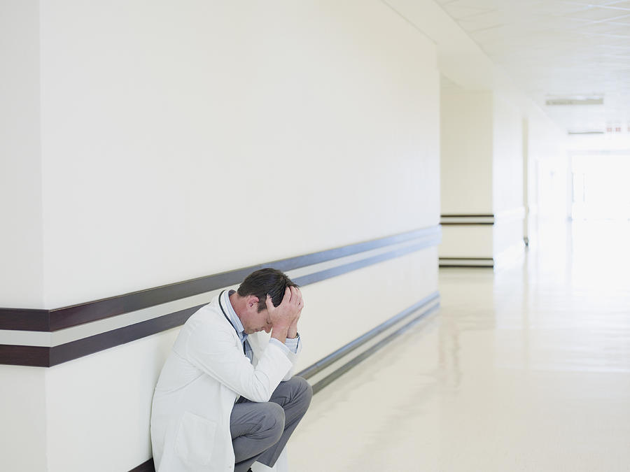Doctor squatting in hospital corridor Photograph by Martin Barraud